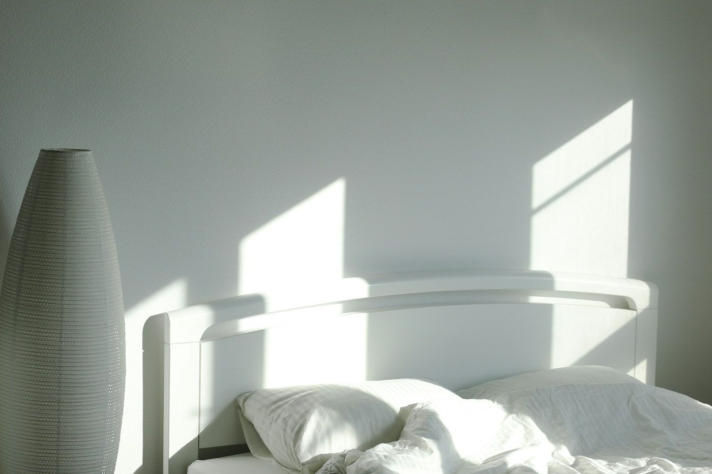 A clean, simply furnished private room with a made bed and soft morning light
